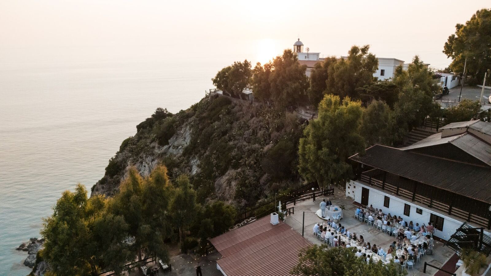 Aerial view of Il Faro at sunset: the lighthouse on the cape, the terraces and the dinner tables