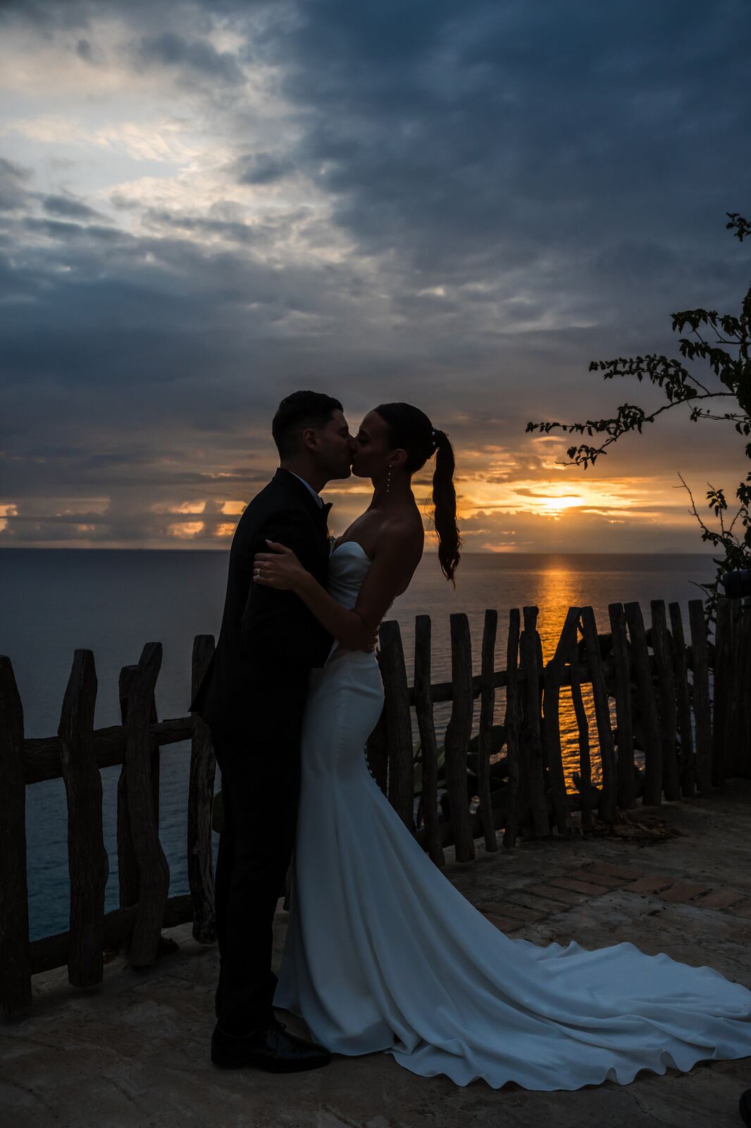 The couple kissing at sunset by the cliff fence